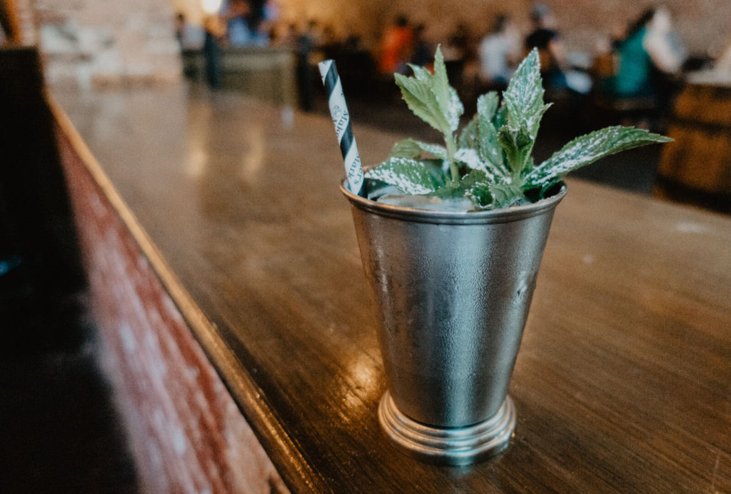 Mint Julep on worn brick wall and paper straw at Merle's Whiskey Kitchen