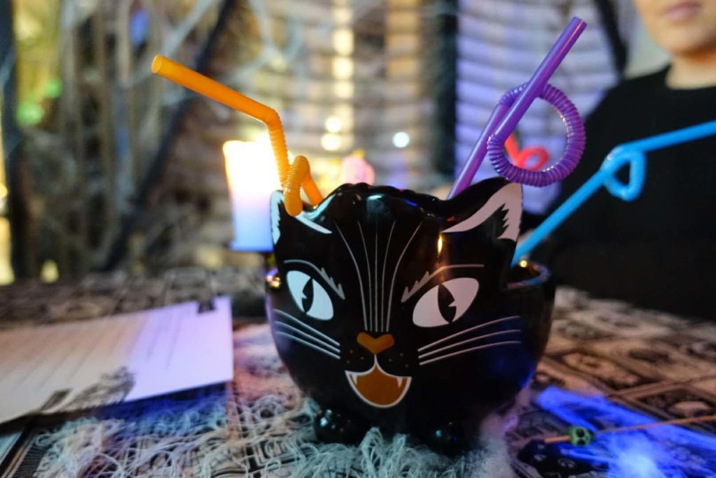 A cat head bowl with three colorful twisty straws poking out of the top at a halloween themed pop-up bar