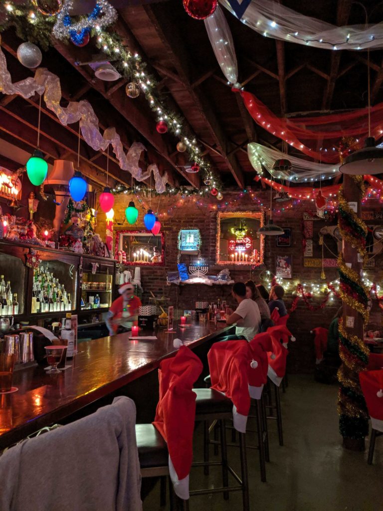 Christmas Lights, colorful fabric, and garland line almost every visible inch of space in this small bar.  There are large christmas light bulbs hanging from the ceiling above the bar.  A menorah is also in the corner.  Every chair is wearing a Santa suit, the bartender is also dressed as Santa. It is the most amazing Christmas bar ever imagined.  
