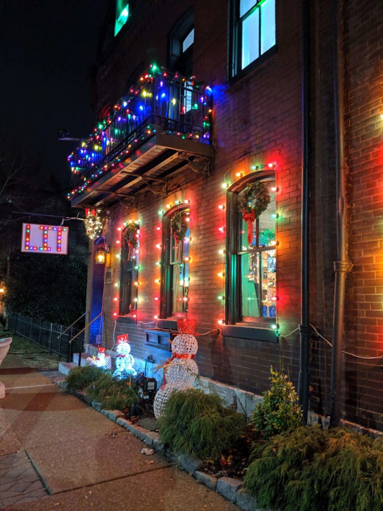 Christmas lights line the windows and balcony of this red brick building.  A small sign with Christmas bulk letters reads "LIT"