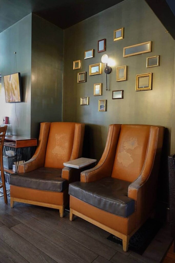 Two faded leather chairs sit side-by-side.  There are 14 tiny mirrors on the wall behind these chairs.  The walls and ceilings are painted dark green. 
