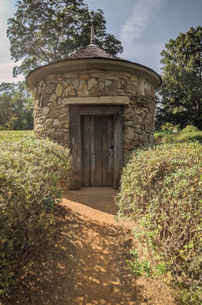 A stone hut at the center of a green hedge maze. 