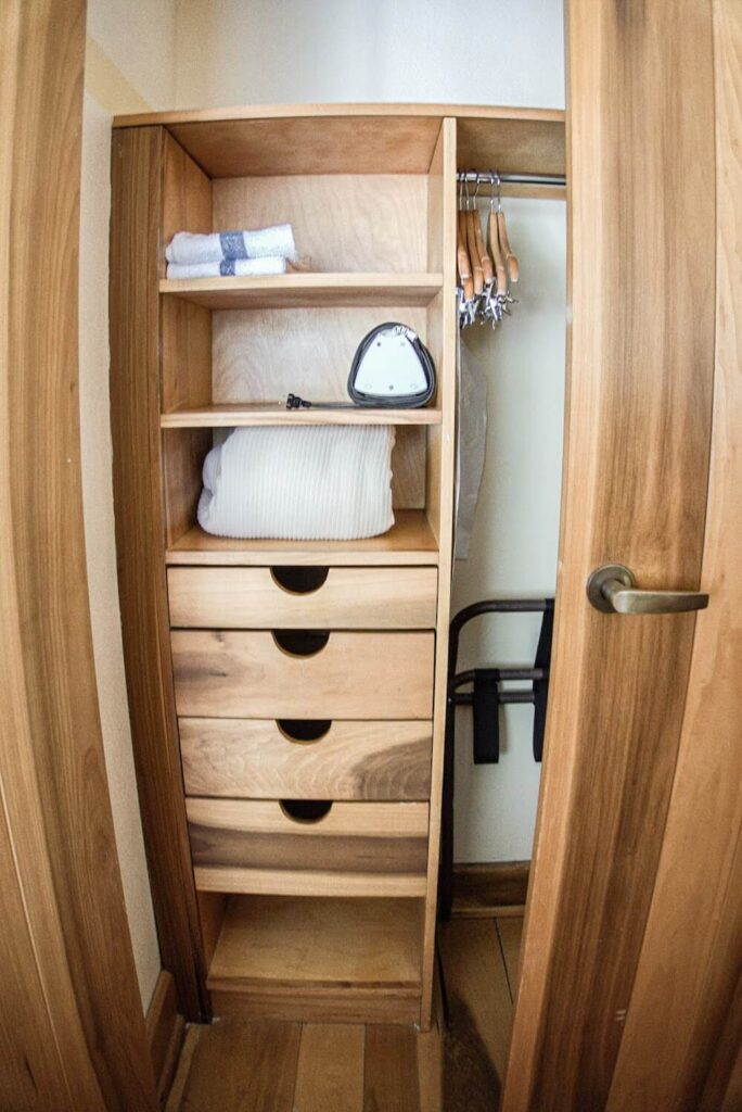 A tall closet with built in drawers from floor to ceiling.  An iron and knit blanket take up two of the shelves.  Empty hangers are on the rod. 