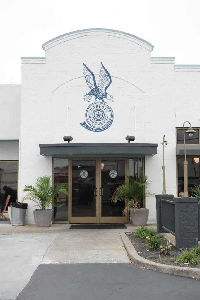 A brick building completely painted white with a large eagle logo painted on the top.  The Eagle in the logo is carrying a circle that looks a little bit like a donut and it reads "Parlor Doughnuts & Coffee"