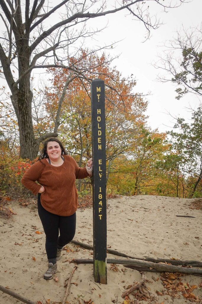 a person standing next to a post that reads "Mt. Holden. Elevation 184 feet"