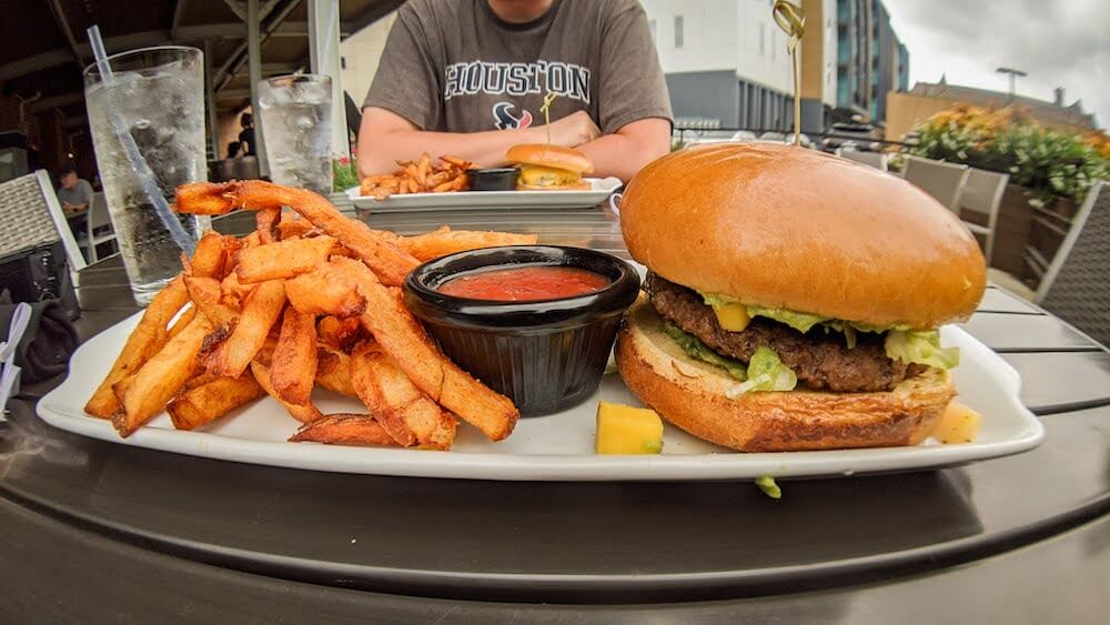 A vegetarian burger made with an impossible burger patty.  The burger is spilling with guacamole and mangoes. there is a pile of french fries next to it. 