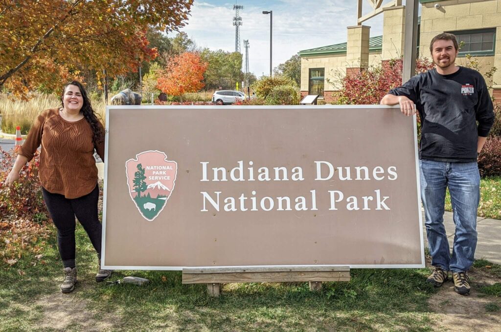 Two people next to the sign that reads Indiana Dunes National Park at the Visitor's Center.