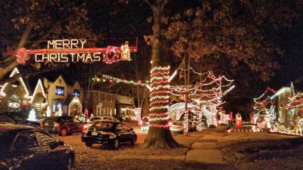 A neighborhood decorated in Christmas lights.  A "Merry Christmas" banner hangs across the street.